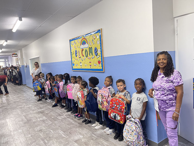 Teacher and her students lined up in the school hallway holding their backpacks