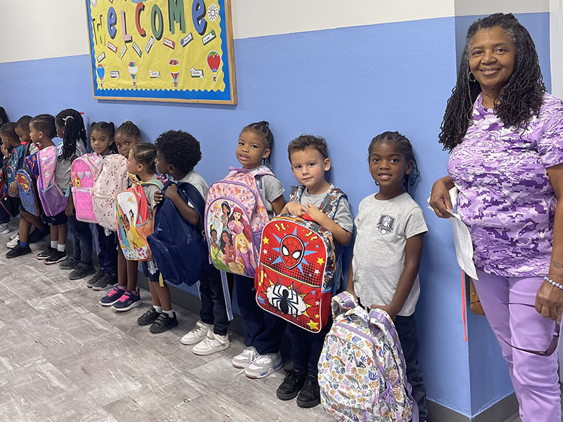 Teacher with her students ready in the hallway to get their backpacks blessed
