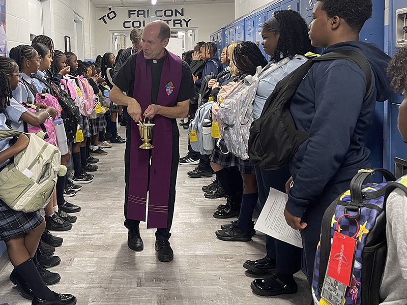 Priest walking down the school hallway to bless backpacks