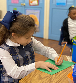 Young school girl in her school uniform working on an assignment at her desk