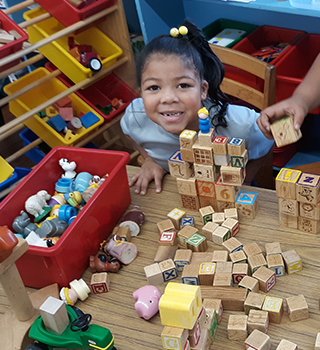 Cute young school girl smiling up from table with blocks